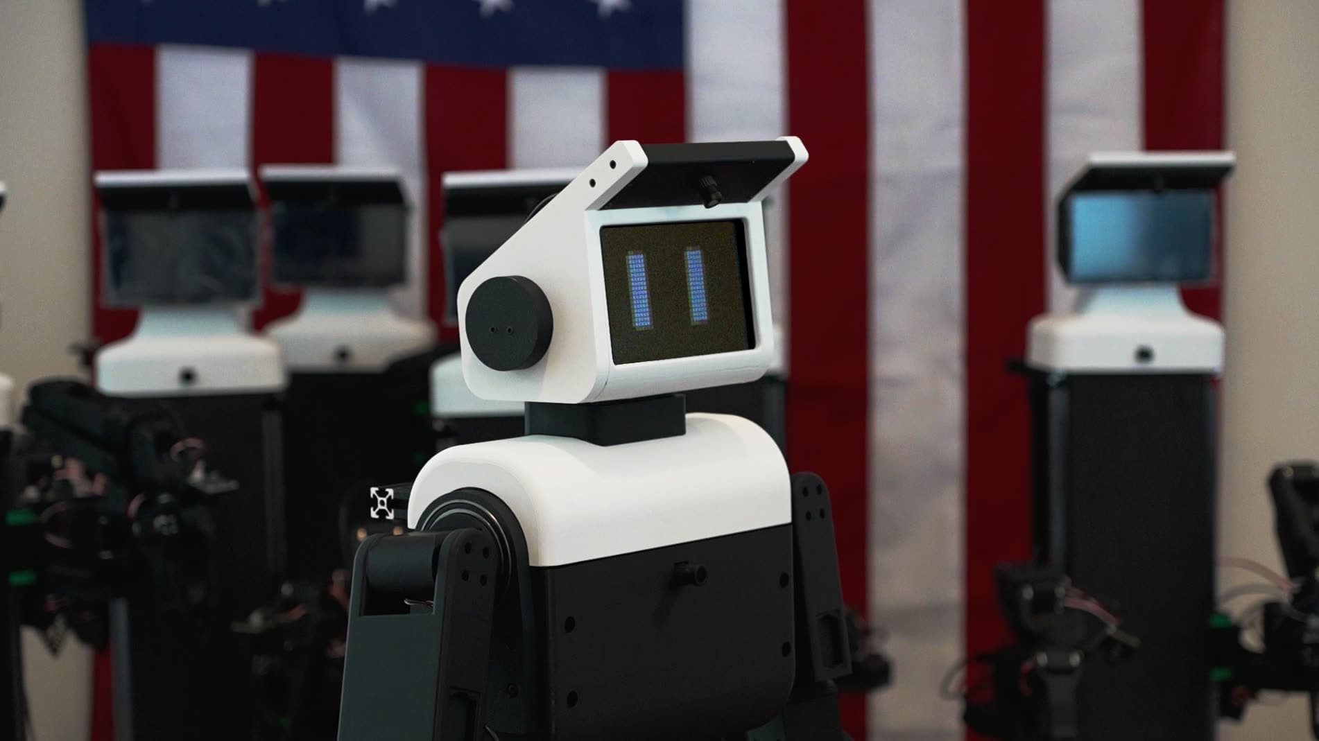 A line of NORI robots in front of an American flag in the San Francisco workshop